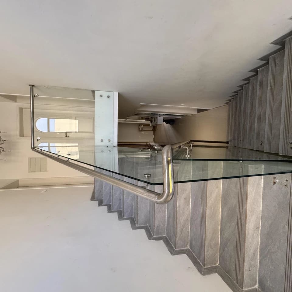 Guarda interior em vidro temperado com passamão em inox junto a uma escada.